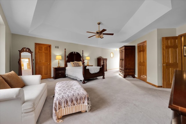 bedroom with ceiling fan, a tray ceiling, and light colored carpet