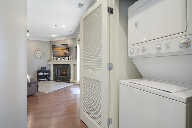 clothes washing area featuring ornamental molding, hardwood / wood-style floors, a tiled fireplace, and stacked washing maching and dryer