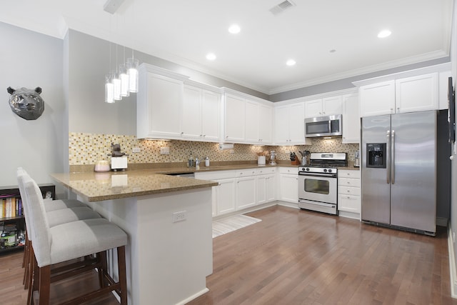 kitchen featuring dark hardwood / wood-style floors, kitchen peninsula, a breakfast bar, white cabinetry, and appliances with stainless steel finishes