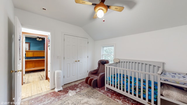 bedroom featuring ceiling fan, wood-type flooring, vaulted ceiling, a closet, and a nursery area