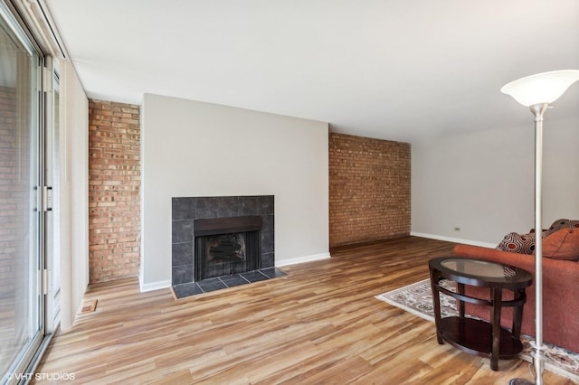 living room with a tiled fireplace, brick wall, and light wood-type flooring