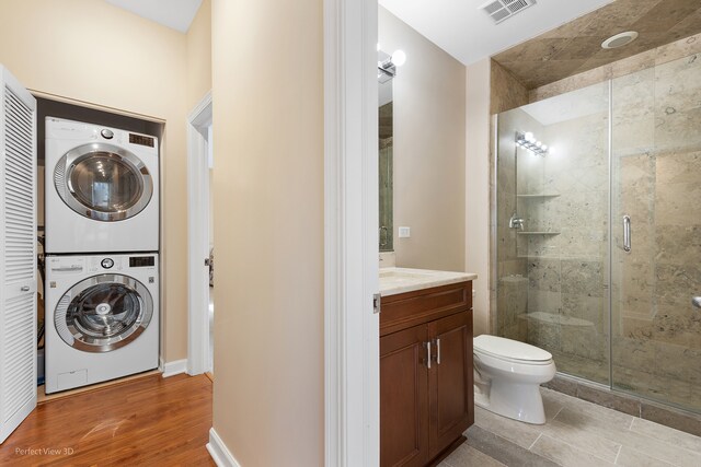 clothes washing area with stacked washer / drying machine and wood-type flooring