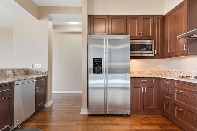 kitchen featuring appliances with stainless steel finishes, dark hardwood / wood-style floors, light stone counters, and wall chimney range hood