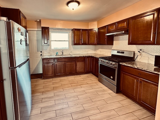 kitchen with sink, light stone counters, ventilation hood, decorative backsplash, and appliances with stainless steel finishes