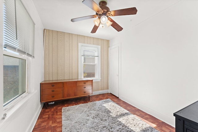 bedroom with ceiling fan, wood walls, and dark parquet floors