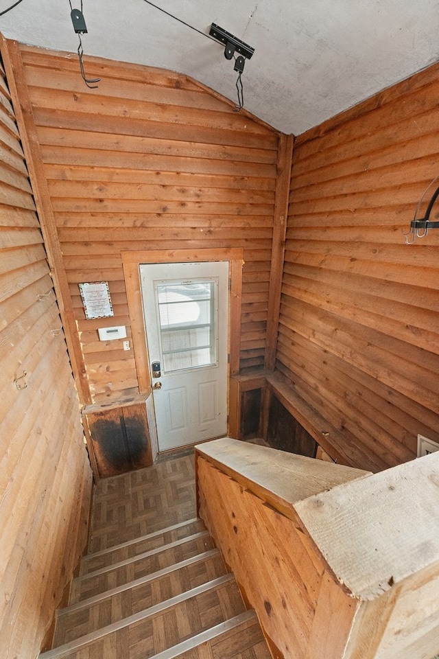 stairway with parquet flooring, wood walls, a textured ceiling, and vaulted ceiling