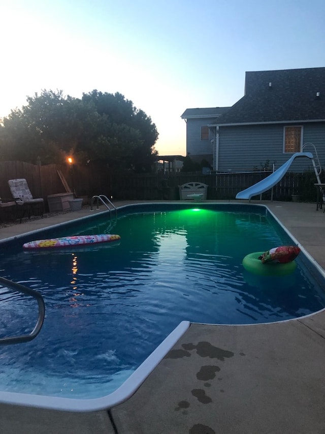 pool at dusk with a water slide and a patio