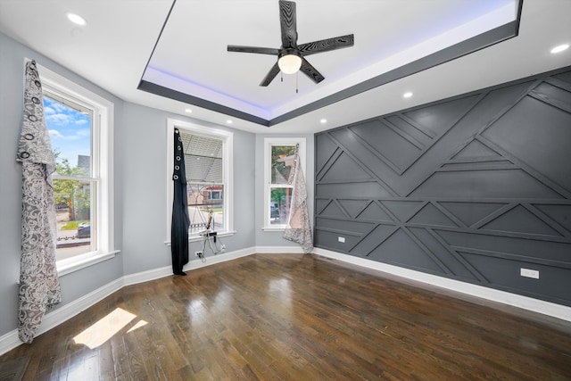 empty room with dark wood-type flooring, ceiling fan, and a raised ceiling