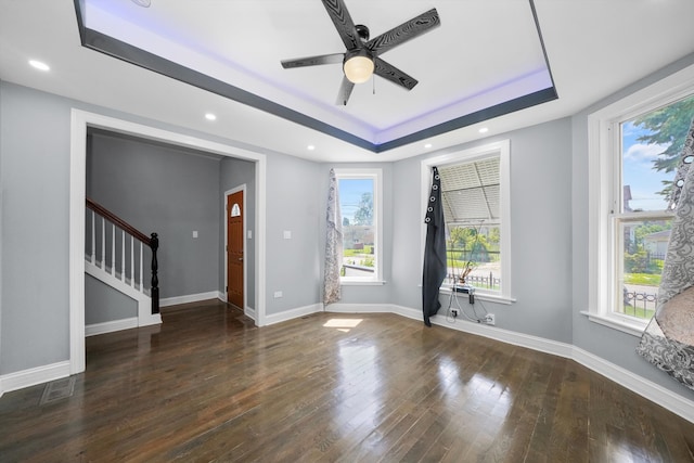 empty room with dark wood-type flooring, a tray ceiling, a healthy amount of sunlight, and ceiling fan