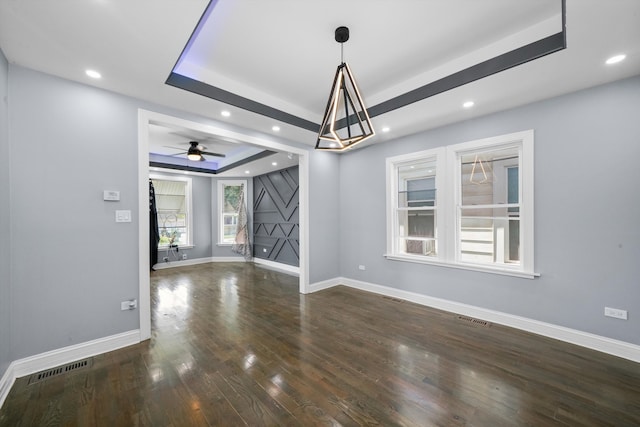 unfurnished room with a tray ceiling, dark hardwood / wood-style floors, and ceiling fan