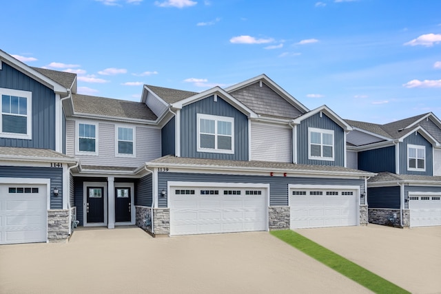 multi unit property with a garage, stone siding, driveway, and board and batten siding