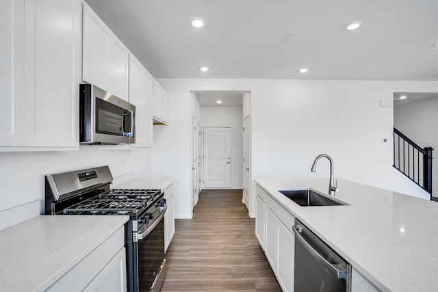 kitchen with light stone counters, stainless steel appliances, recessed lighting, a sink, and wood finished floors