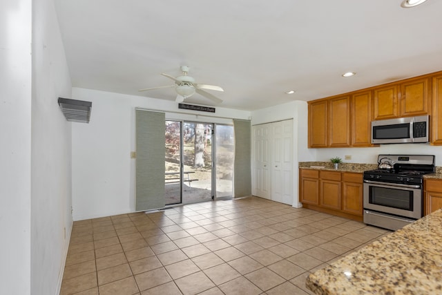 kitchen featuring light tile patterned flooring, light stone countertops, stainless steel appliances, and ceiling fan