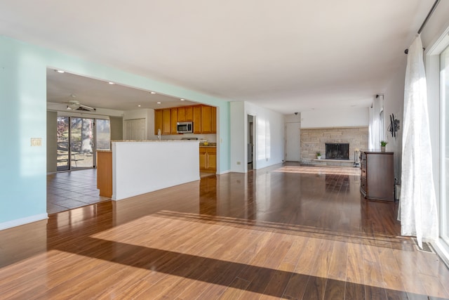 unfurnished living room with a stone fireplace, hardwood / wood-style floors, and ceiling fan