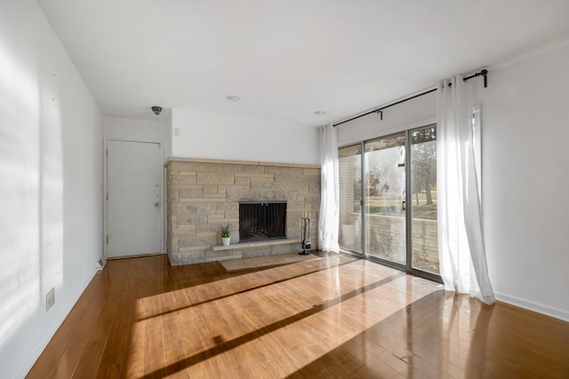 unfurnished living room featuring hardwood / wood-style flooring and a stone fireplace