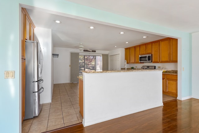 kitchen with light hardwood / wood-style flooring, a kitchen island with sink, stainless steel appliances, and light stone countertops