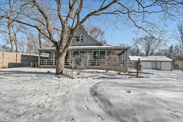 snow covered rear of property featuring an outbuilding, covered porch, and a garage