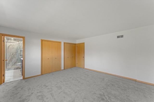 unfurnished bedroom with ensuite bath, light carpet, and two closets