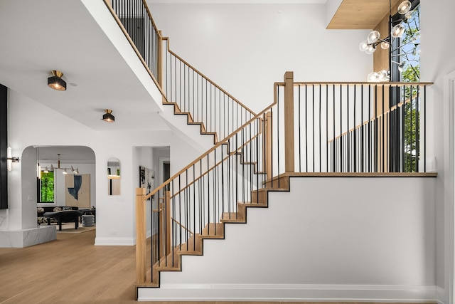 staircase with a wealth of natural light, wood-type flooring, and an inviting chandelier