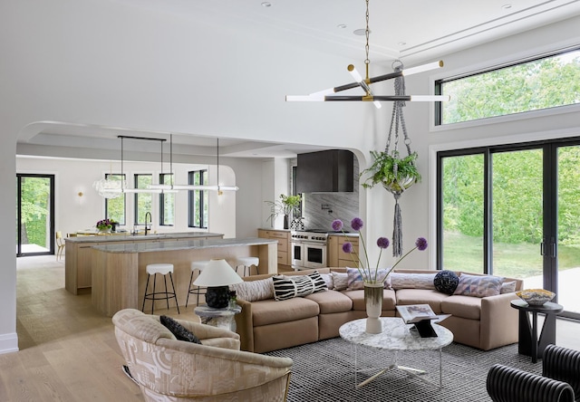 living room with sink, a towering ceiling, light hardwood / wood-style floors, and a notable chandelier