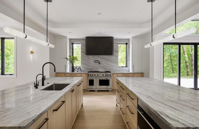 kitchen featuring high end range, a large island with sink, light stone countertops, and sink