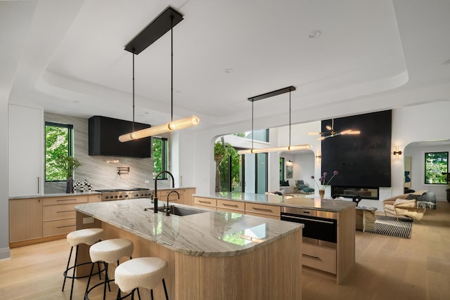 kitchen featuring sink, light stone countertops, hanging light fixtures, and a kitchen island with sink