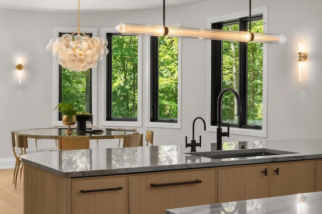 kitchen with pendant lighting, dark stone countertops, sink, and light hardwood / wood-style flooring