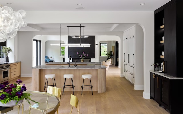 kitchen with light stone counters, light hardwood / wood-style flooring, a chandelier, a breakfast bar area, and a kitchen island with sink