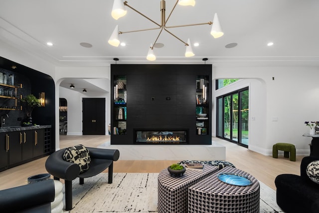 living room featuring a tile fireplace, light hardwood / wood-style flooring, a chandelier, and sink