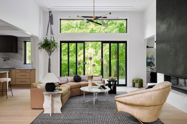 living room featuring light wood-type flooring, a towering ceiling, plenty of natural light, and a notable chandelier