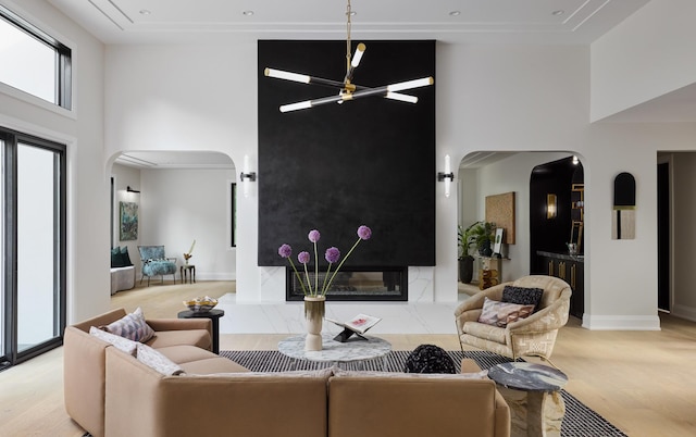 living room featuring a high end fireplace, a towering ceiling, light hardwood / wood-style floors, and a notable chandelier