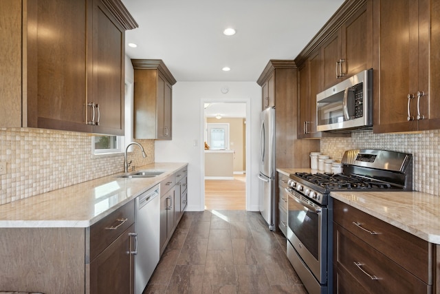 kitchen with sink, decorative backsplash, light stone counters, appliances with stainless steel finishes, and dark hardwood / wood-style flooring