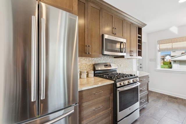 kitchen featuring stainless steel appliances, light stone countertops, decorative backsplash, and dark tile patterned flooring