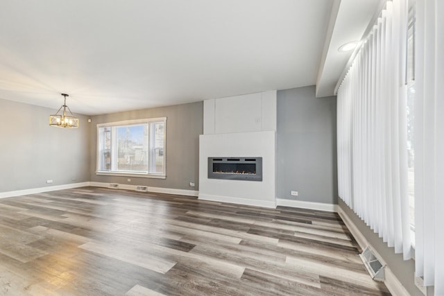 unfurnished living room featuring heating unit, hardwood / wood-style floors, a large fireplace, and an inviting chandelier