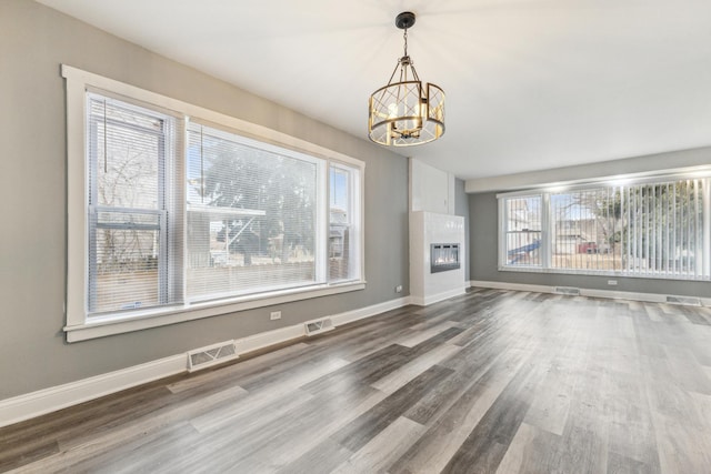 unfurnished living room with a tiled fireplace, hardwood / wood-style floors, and a notable chandelier