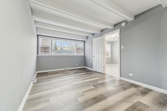 spare room featuring beam ceiling and light hardwood / wood-style flooring