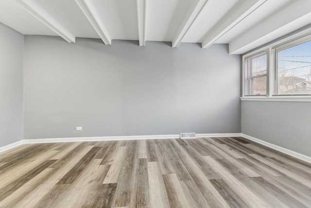 spare room with beam ceiling and light hardwood / wood-style flooring