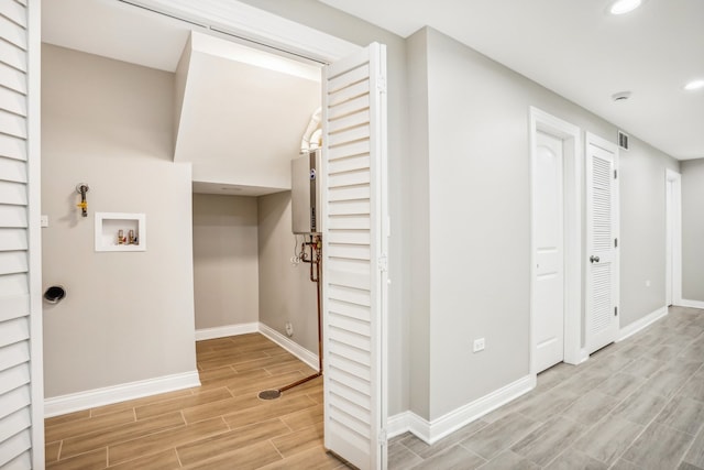 laundry room with water heater, light hardwood / wood-style flooring, and hookup for a washing machine