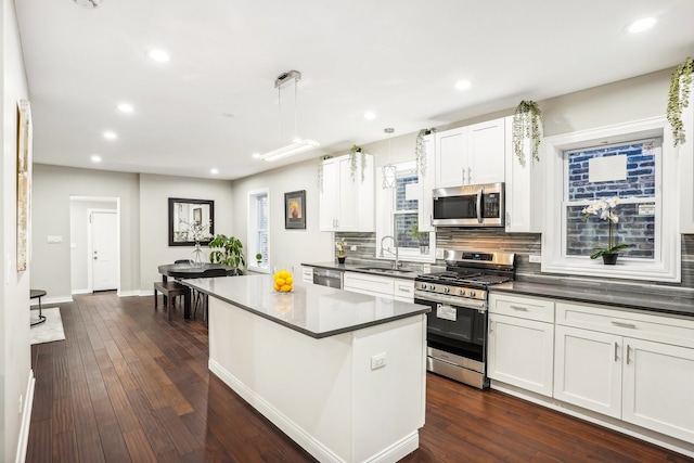 kitchen with white cabinets, dark hardwood / wood-style flooring, appliances with stainless steel finishes, a kitchen island, and decorative light fixtures