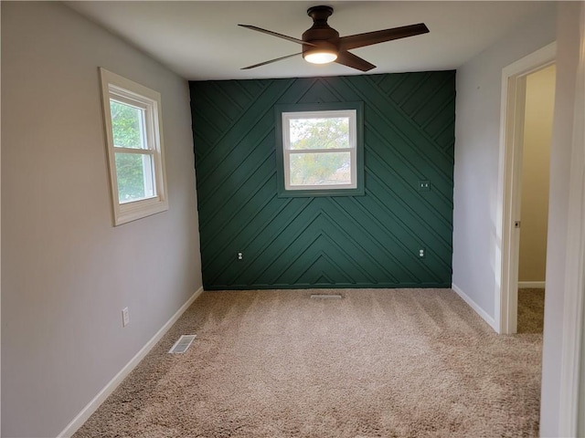 carpeted empty room featuring wood walls, a healthy amount of sunlight, and ceiling fan