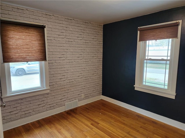 spare room featuring brick wall and hardwood / wood-style floors