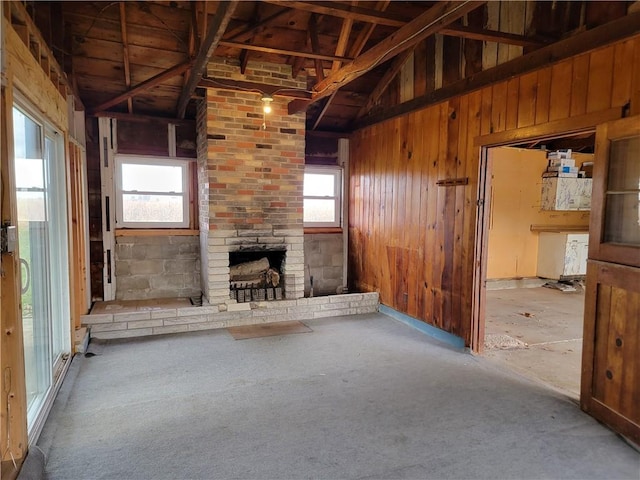 unfurnished living room with a healthy amount of sunlight, lofted ceiling, wooden walls, and a stone fireplace