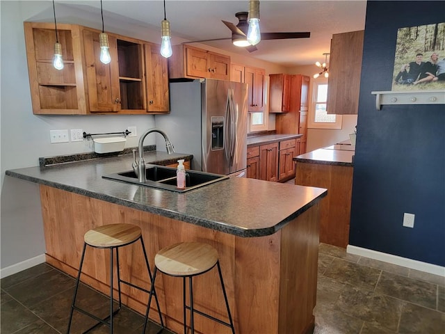 kitchen featuring kitchen peninsula, stainless steel fridge, hanging light fixtures, a kitchen bar, and sink