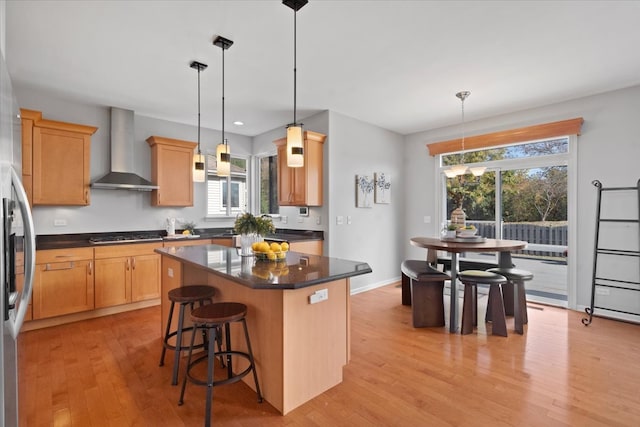 kitchen with light wood-type flooring, a kitchen island, plenty of natural light, and wall chimney exhaust hood