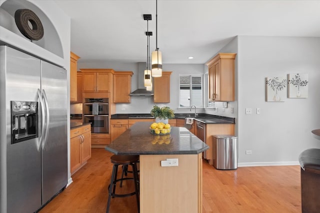 kitchen featuring stainless steel appliances, wall chimney range hood, light hardwood / wood-style flooring, a kitchen island, and hanging light fixtures