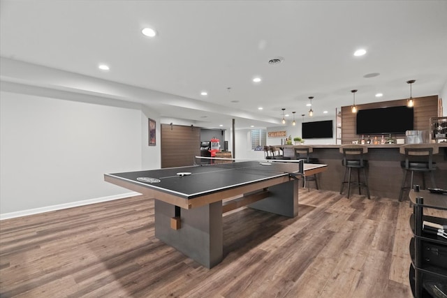 game room with a barn door, hardwood / wood-style flooring, and bar