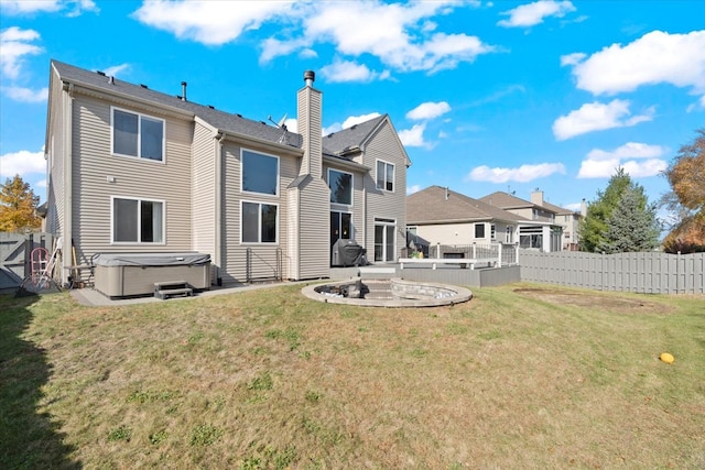 rear view of property featuring a yard, a patio, and a hot tub