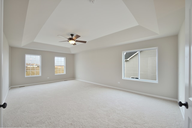 empty room featuring light carpet, a raised ceiling, and ceiling fan