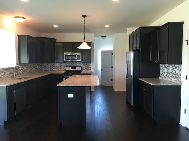 kitchen featuring a kitchen island, dark hardwood / wood-style floors, pendant lighting, appliances with stainless steel finishes, and light stone counters