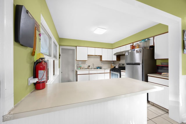 kitchen featuring kitchen peninsula, stainless steel appliances, white cabinets, decorative backsplash, and light tile patterned floors